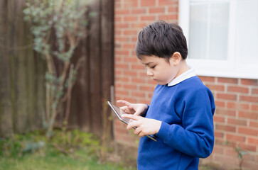 Wall Mural - Happy Child boy holding tablet pc standing outside waiting for School bus, Portrait Kid playing game online or reading strory on internet, Preschool boy learning with modern technology