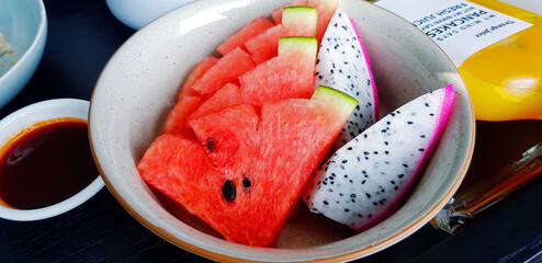 Wall Mural - Close up fresh sliced of watermelon and dragon fruit in plate with bottle of orange juice on black wooden table. Freshness fruit in dish on wood background. Set of Healthy food and Diet