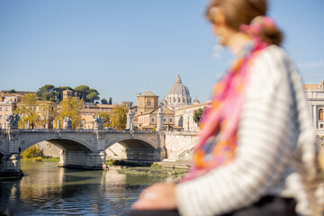 Canvas Print - Woman enjoying beautiful view of Rome city and Vatican standing on the bridge on a sunny autumn day. Elegant woman wearing stripped blouse and shawl in hair. Focus on background