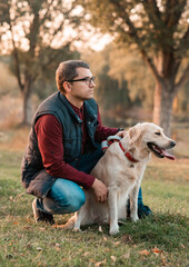 Wall Mural - Young man hugging golden retriever dog in autumn outdoors