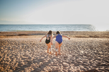 Wall Mural - Two children of girls in swimsuits run on the sand and play on the beach. Summer holidays and adventures of siblings. Active games on the sea coast. overweight child