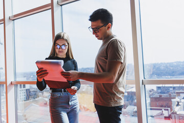 Wall Mural - A young business woman with documents in glasses stands with a male manager while holding a corporate business meeting in a modern office. Business meeting concept. Free space, selective focus