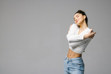 Happy woman hugging herself with natural emotional enjoying face with closed eyes on blue background. Love concept of yourself.