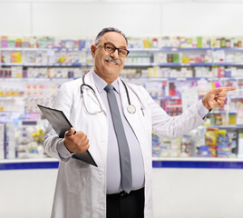 Poster - Smiling mature pharmacist standing with a clipboard and pointing in a pharmacy