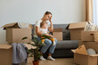 © sementsova321 - Portrait of sad tired Caucasian woman wearing white t shirt sitting on sofa, being surrounded with carton parcels needs to uncase, expressing sadness, moving day.