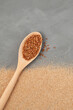 Organic buckwheat in wooden spoon and Buckwheat coarse flour (ground grits) or flake on grey textured surface