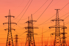 Background, View Or Scene Of Steel Tower Of Electric Main Or Electricity Transmission Line With The Wires Silhouette On Yellow, Orange And Red Background Of Sunset Or Sunrise Sky