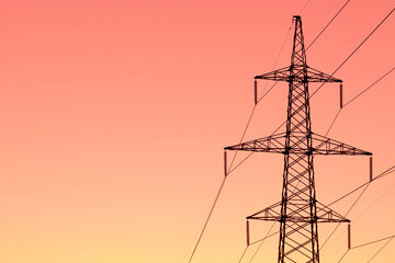 Background, view or scene of steel tower of electric main or electricity transmission line with the wires silhouette on yellow, orange and red background of sunset or sunrise sky