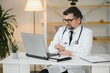 © Serhii - Portrait of a serious doctor using laptop in medical office