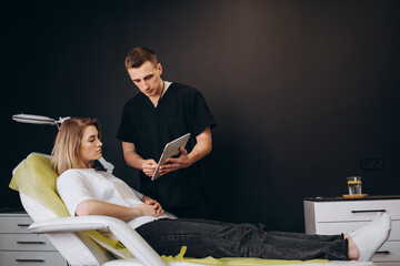 Wall Mural - Plastic, Cosmetic Surgeon Consults Woman about Facial Lift Surgery, He Draws Arrows on Digital Tablet Computer Screen, Showing Types of Facelift and Nose Correcting Procedures Available for Her.