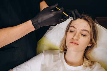 Wall Mural - Portrait of young Caucasian woman getting botox cosmetic injection in forehead. Beautiful woman gets botox injection in her face.