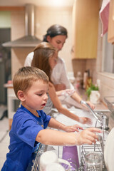 Sticker - Many hands at work. Shot of a little boy washing dishes with his family at a kitchen sink.