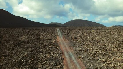 Wall Mural - Drone point of view Timanfaya National Park, rocky volcanic landscape and mountains on blue cloudy sky background. Canary Islands, Lanzarote, Spain. Travel destination, famous places concept	