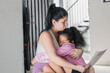 beautiful latina woman hugging her daughter while reading the letter her daughter gave her as a gift. tender moment between mother and daughter sitting on the floor of their home. concept of home.