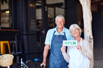 Poster - Come on down and see what we have to offer. Portrait of a happy senior couple holding up an open sign in their store.