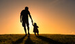 Silhouette of father holding his child's hand walking into the sunset. Fatherhood, parenting concept. 