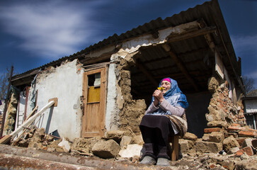 War in Ukraine. Grandmother prays for an end to the war. Ukrainian refugees. A woman in front of a house destroyed by a rocket. Consequences of the war in Ukraine. Ukrainian woman prays for peace.