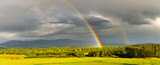 Fototapeta Tęcza - A storm front with numerous rainfalls passes over the mountains, the sun came out from behind the clouds, a colorful rainbow against the background of dark clouds.