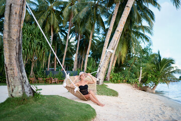 Poster - Vacation concept. Enjoying the summer. Young pretty woman in hat and swimwear laying in hammock on the beach.