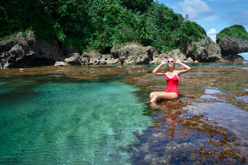 Wall Mural - Summer vacation. Young woman in red swimsuit bathing at sea natural pool.