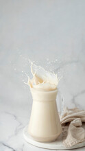 No-dairy Plant Milk Splashes In Glass Jug On White Marble Background