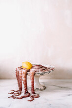 An Octopus And A Lemon In An Old And Decorated Footed Dish, The Tentacles Falling Outside On A Marble Table.