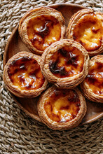 Top View Of Some Pasteis De Nata (small Traditional Portuguese Cake) In A Wooden Plate, On A Natural Fiber Trivet