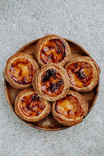 Six Pasteis De Nata (small Traditional Portuguese Cake) Placed On A Wooden Plate, On Grey Ciment Background. Top View