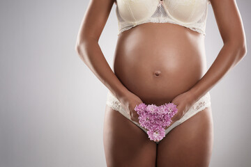 Wall Mural - She blossoms with new life inside her. Studio shot of an unrecognizable pregnant woman holding flowers against a gray background.