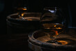Brandy-alcoholic drink stands on wooden barrel full of brandy illuminated by soft dim light in style of rustic. Old barrel of cognac stands in wine cellar. Wine alcoholic strong drink brandy.