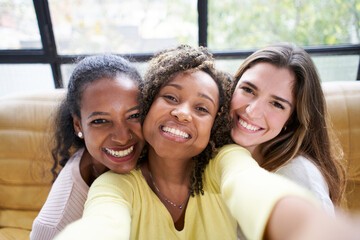 Wall Mural - Three beautiful happy young woman taking smiling selfie looking. at the camera at home. Cheerful female people family and friends together