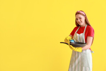 Wall Mural - Young woman with sponge and dirty frying pan on color background