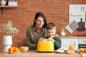 little boy with his mother putting bread slices into toaster in kitchen