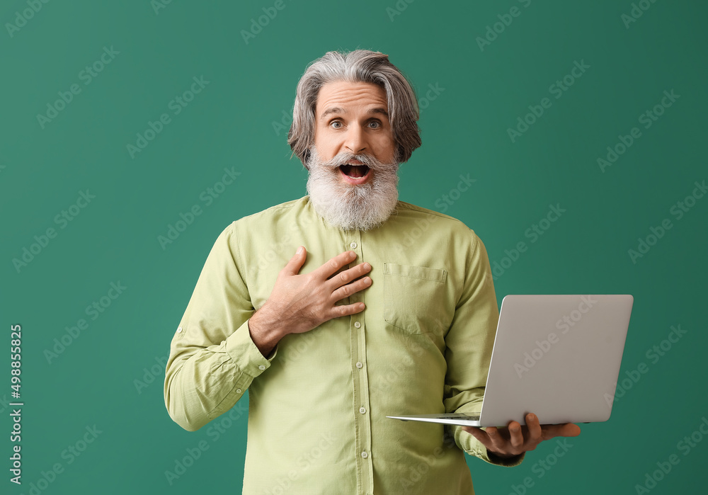 Surprised senior man with laptop on green background