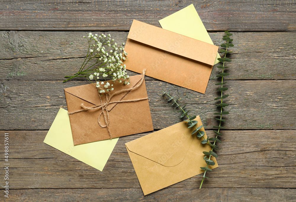 Envelopes with cards, flowers and eucalyptus branches on wooden background