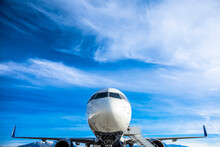 Close Up View Of The Front On An Airplane Sitting At The Airport With Clouds And Sky In The Background. Good Generic Air Travel Photo.