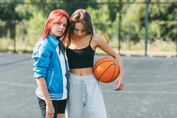 Portrait of two charming girls with a basketball on the sports field. Friendship, best friends, sports