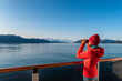© Maridav - Vacation adventure. Alaska Glacier Bay cruise ship passenger looking at Alaskan mountains with binoculars exploring Glacier Bay National Park, USA. Woman on travel Inside Passage enjoying view