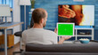 © DC Studio - Back view of man holding digital tablet with green screen watching social media video content sitting on sofa. Person looking at touchscreen device with chroma key looking at influencer vlog.