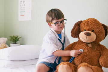 Sticker - Help them find their aspirations. Shot of a little boy pretending to be a doctor while examining his teddybear.