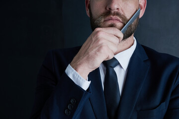 Poster - In my business, it pays to look polished. Shot of an unidentifiable businessman grooming his beard with a comb against a dark background.