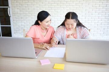 Wall Mural - down syndrome teenage girl and her teacher studying and writing about math on paper with laptop computer for education