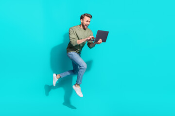 Wall Mural - Full length photo of millennial blond guy jump type laptop wear sweater jeans shoes isolated on turquoise background