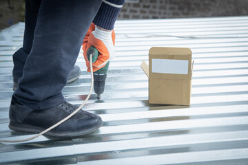 Wall Mural - Man installing metal sheet roof by electrical drilling machine.