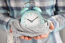 Lady Hold Green Alarm Clock, Changing Time From Summer To Winter, Clock Wrapped In Knitted Scarf