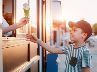 child a little boy buys ice cream in a green waffle cup on the street from an ice cream maker in hot summer