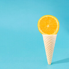 Wall Mural - Orange in ice cream cone. Summer coming design idea. Aesthetic refreshment on a sky blue background. Fruity ice cream making sunny day shadow