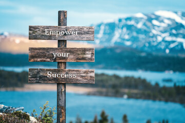 empower your success text quote written on wooden signpost outdoors in nature with lake and mountain scenery in the background. Moody feeling.
