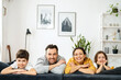 © Vadim Pastuh - Happy multiracial family of four laying at the sofa in cozy living room, parents and kids laughing. Family feeling happy during the weekend