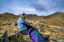 A Woman Hiker Smiling At The Camera, Framed By The Helvellyn Ridges In The Background, Shot In Landscape